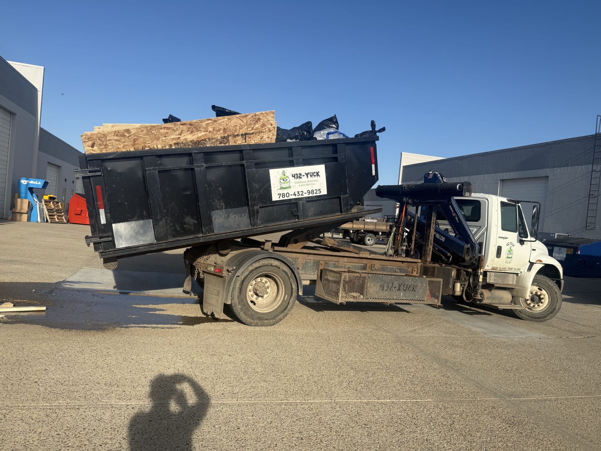 A heavy-duty truck hoisting a green waste container during a residential bin delivery in Edmonton.