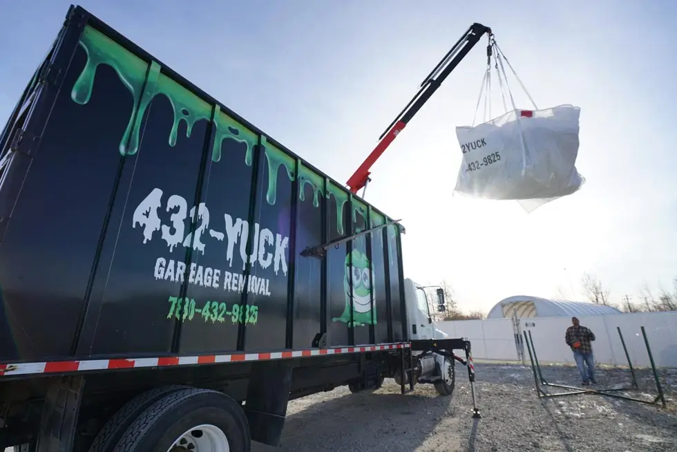 A specialized crane arm loading heavy materials into a high-walled green waste trailer in Edmonton.